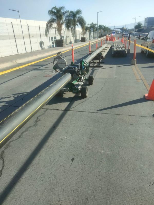 Tubería de polietileno negra con franja amarilla sobre una máquina de termofusión, en un carril confinado con conos de una avenida industrial
