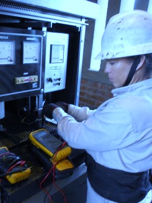 Técnica con casco midiendo con dos multímetros en el tablero de control de una estación