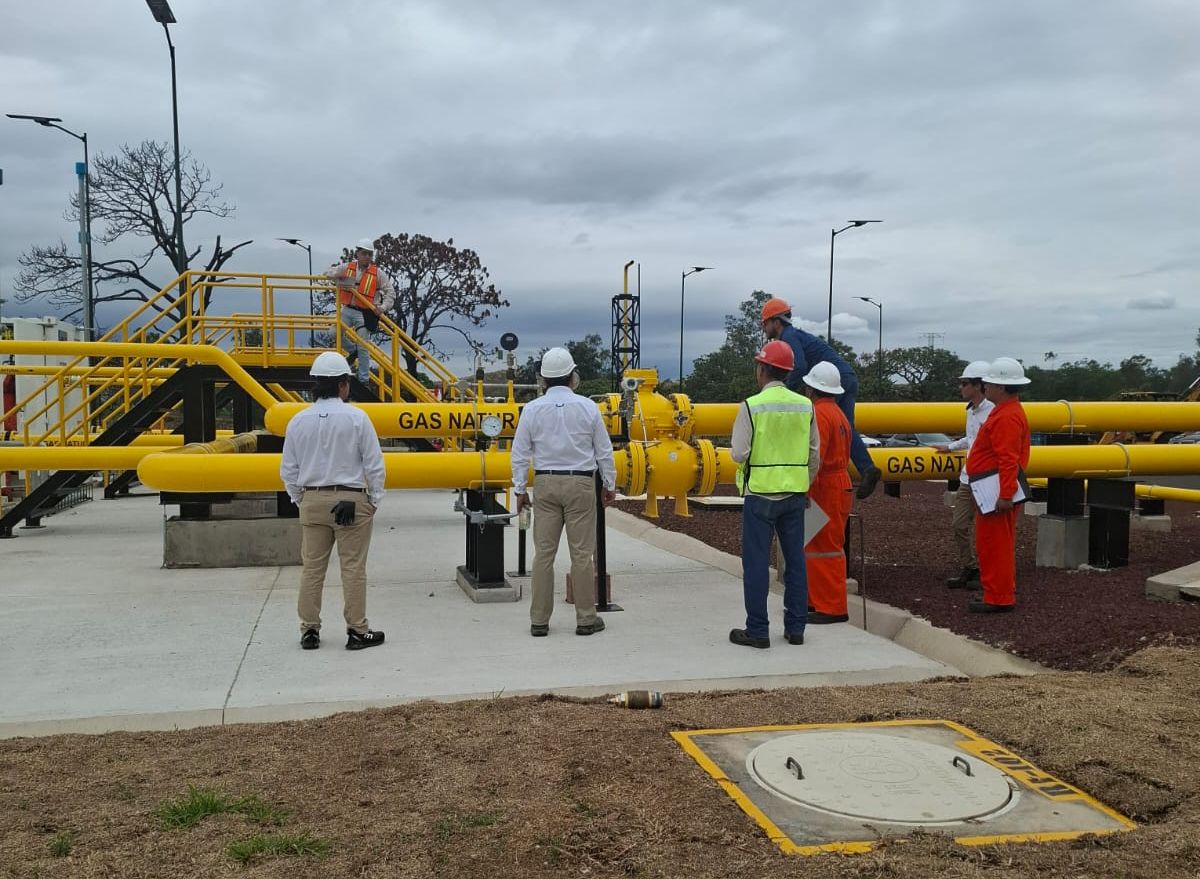 Recorrido técnico en una estación de gas natural: personal con casco y equipo de protección junto a la tubería amarilla